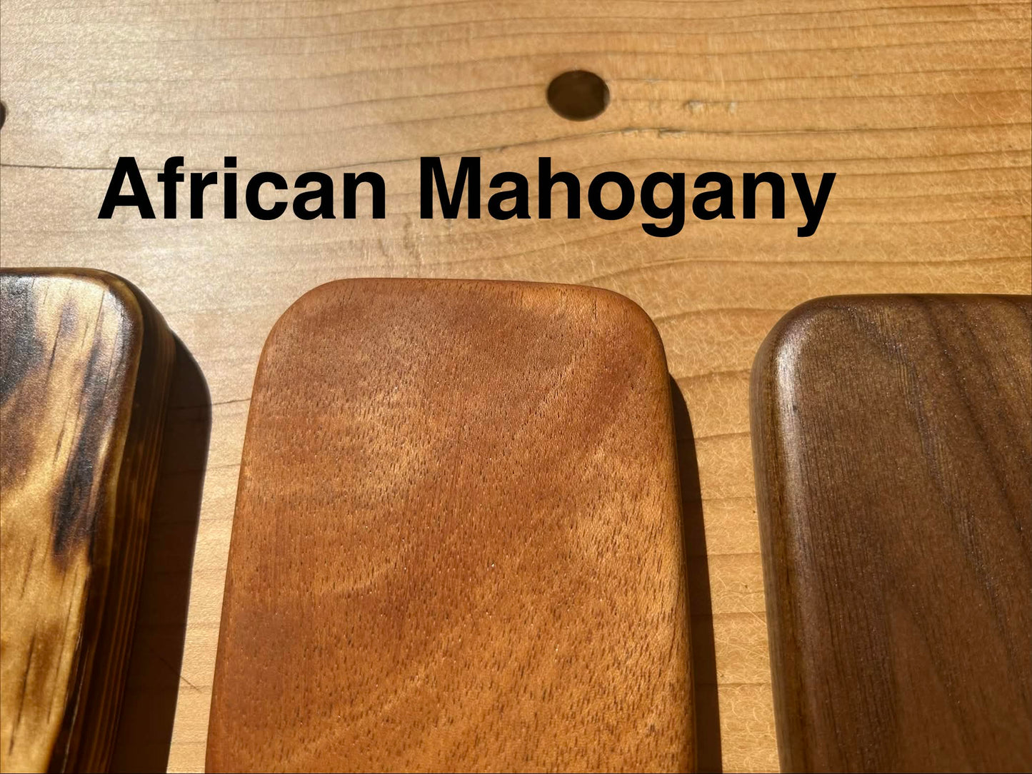 Three wooden paddles with 'African Mahogany' text on a wooden workbench
